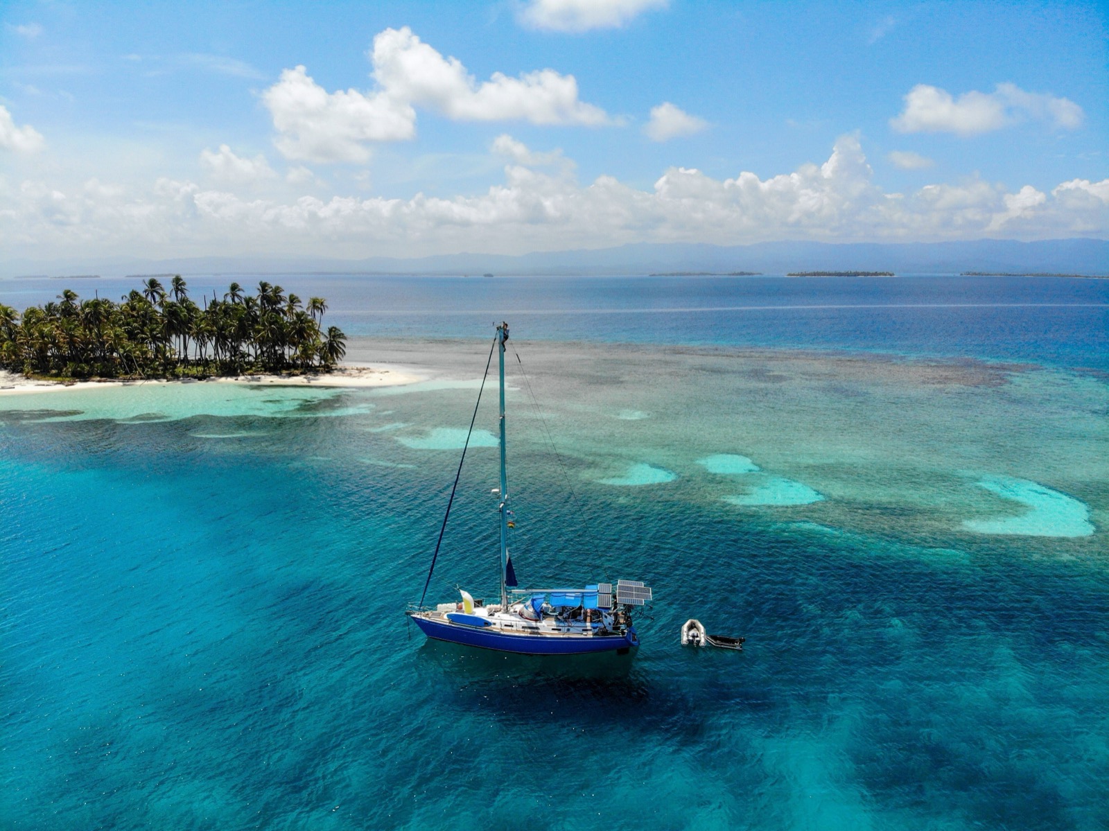 Jacht na kotwicy przy rafie, obok wyspy z palmami, archipelag San Blas